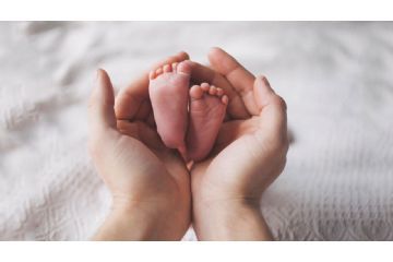 Mani di un adulto che avvolgono i piedini di un neonato